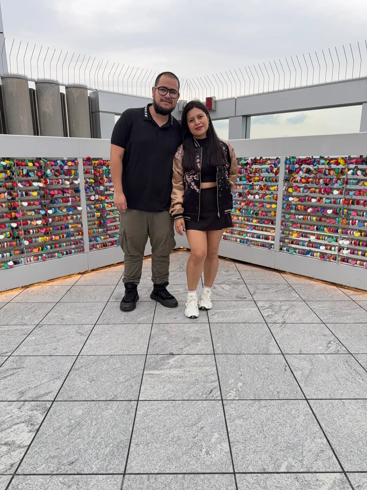 Ariadna y Rogelio en una terraza mirador, frente a un muro de candados de colores
