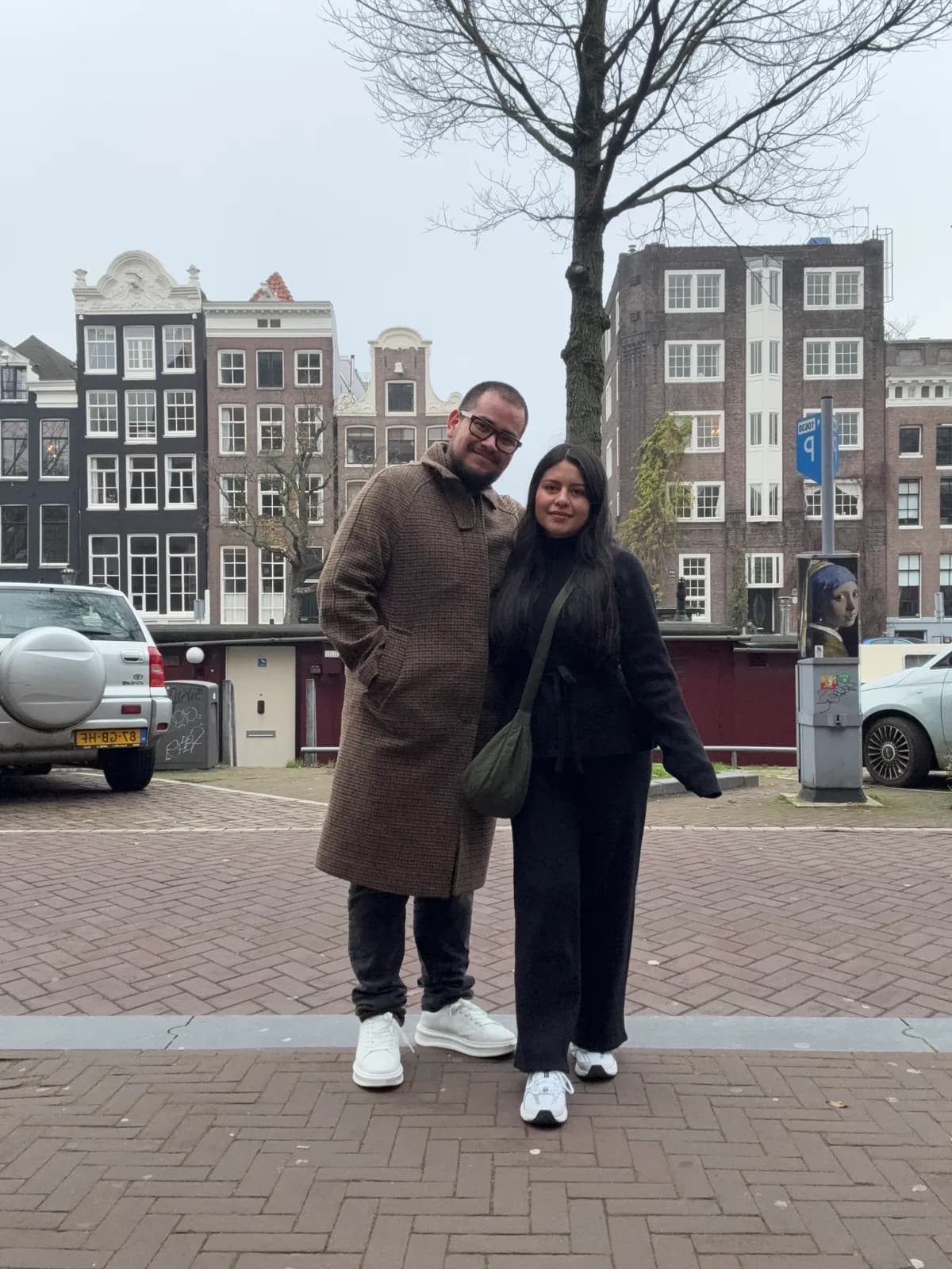 Ariadna y Rogelio abrazados en una calle de Ámsterdam, con las casas del canal al fondo