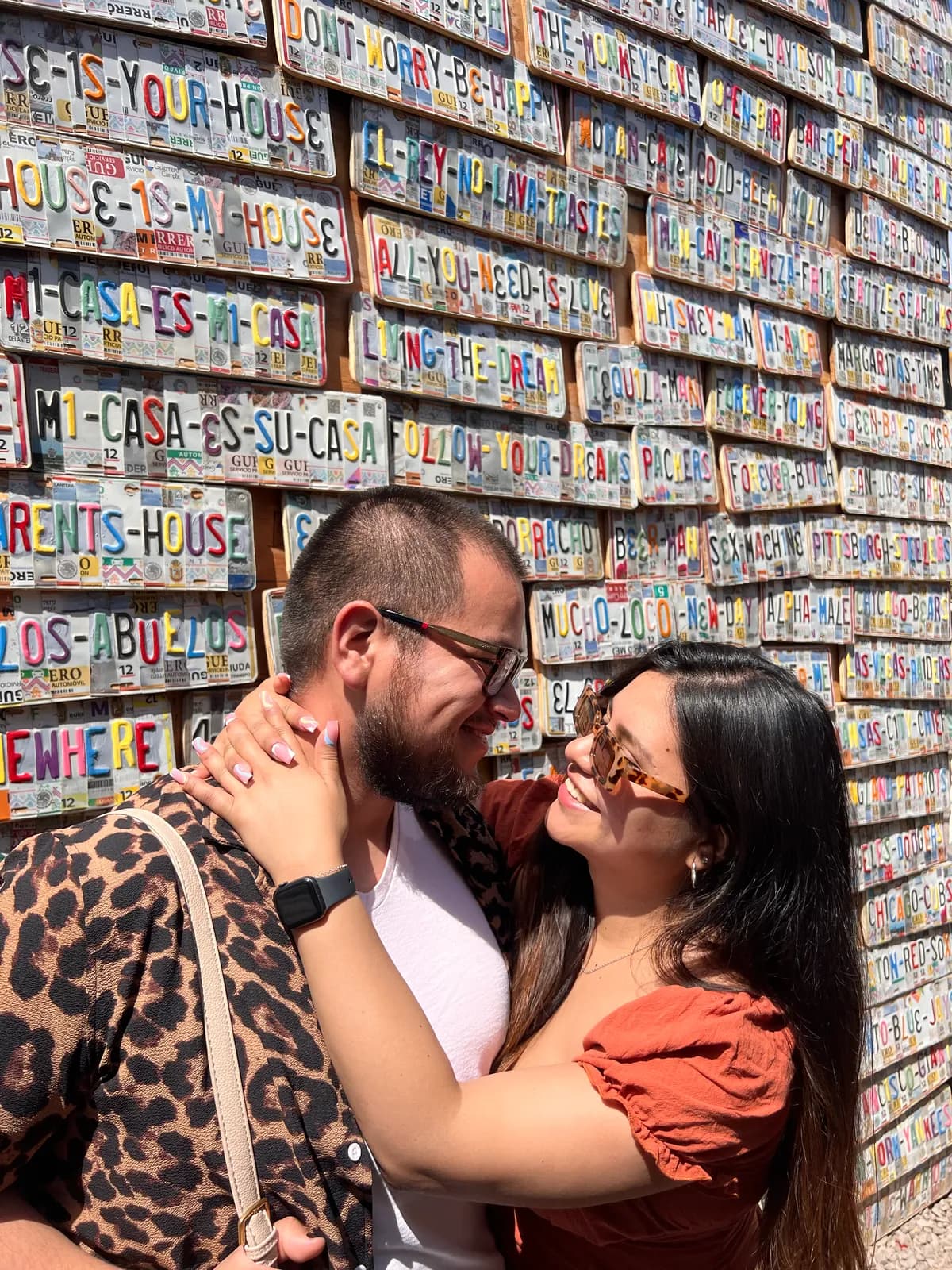 Ariadna y Rogelio mirándose con complicidad frente a un muro de placas de colores